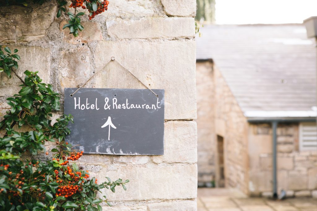 Petite ardoise "Hôtel & Restaurant" accrochée sur un mur en pierre dans un village